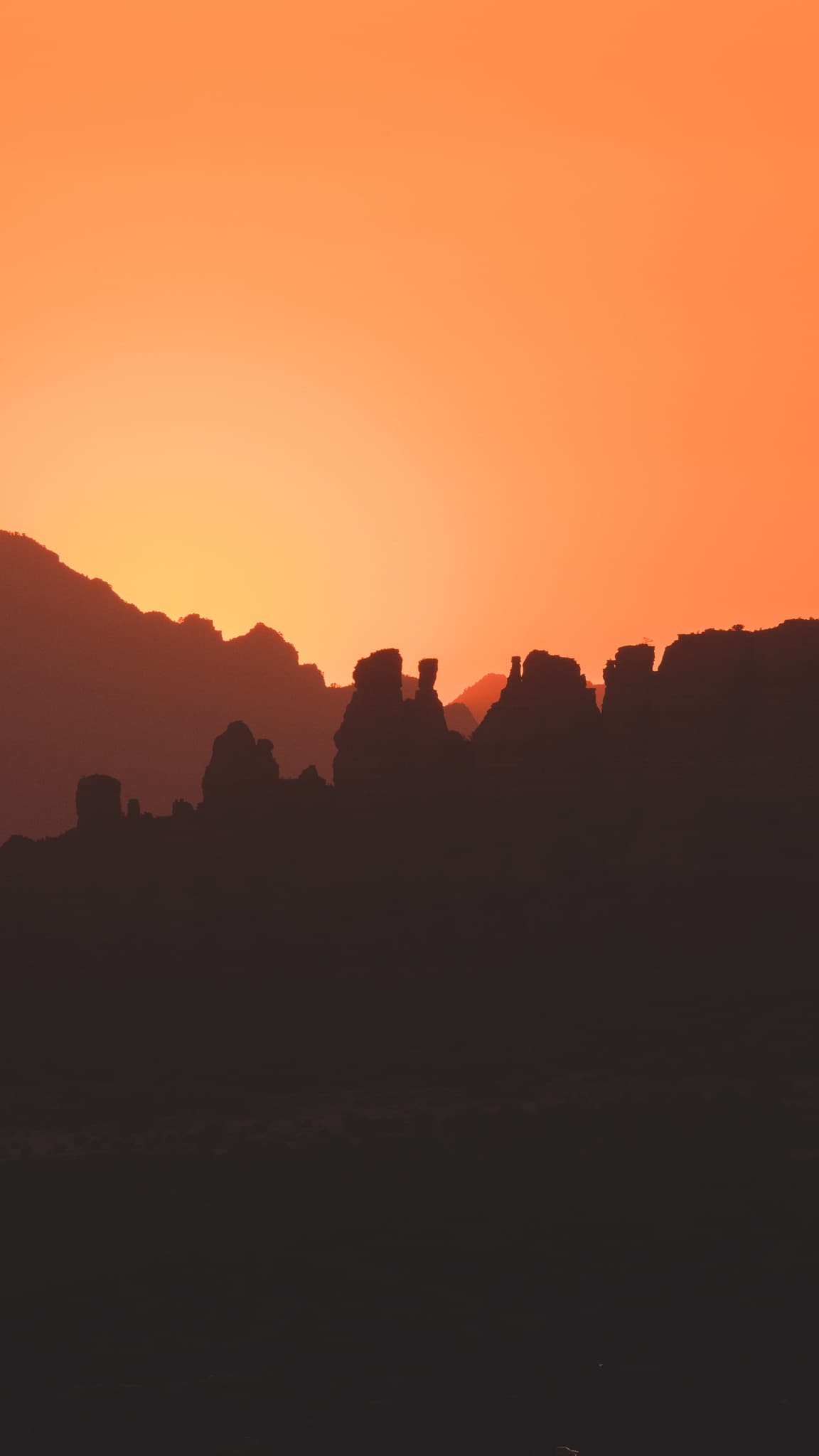 A silhouette of rocky formations against a vibrant orange sunset sky