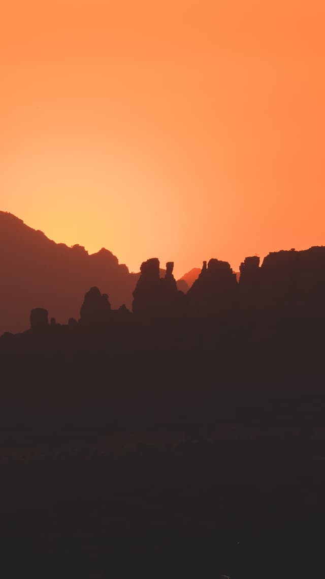 A silhouette of rocky formations against a vibrant orange sunset sky
