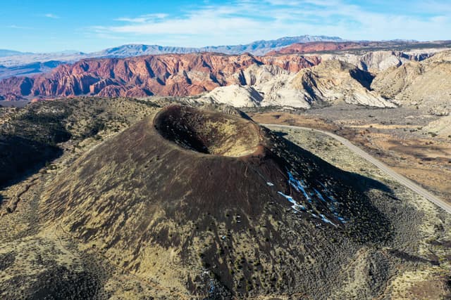 Aerial view of a volcanic crater surrounded by rugged terrain with colorful rock formations in the background