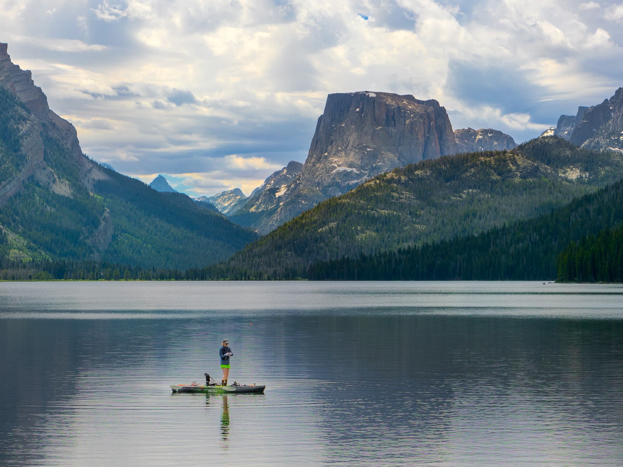 A serene lake surrounded by mountains with a person standing on a paddleboard in the center