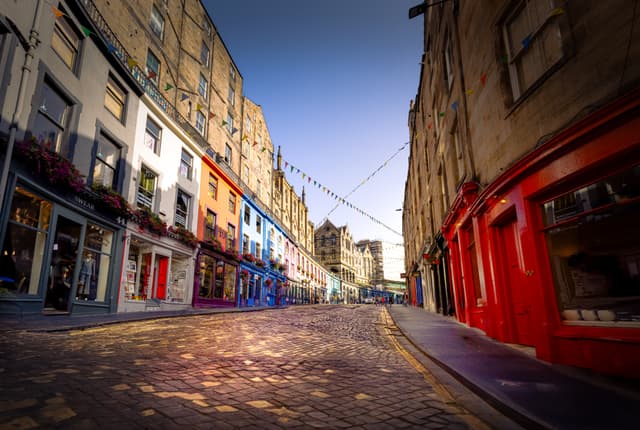 A cobblestone street lined with colorful buildings, including shops and cafes, under a clear blue sky