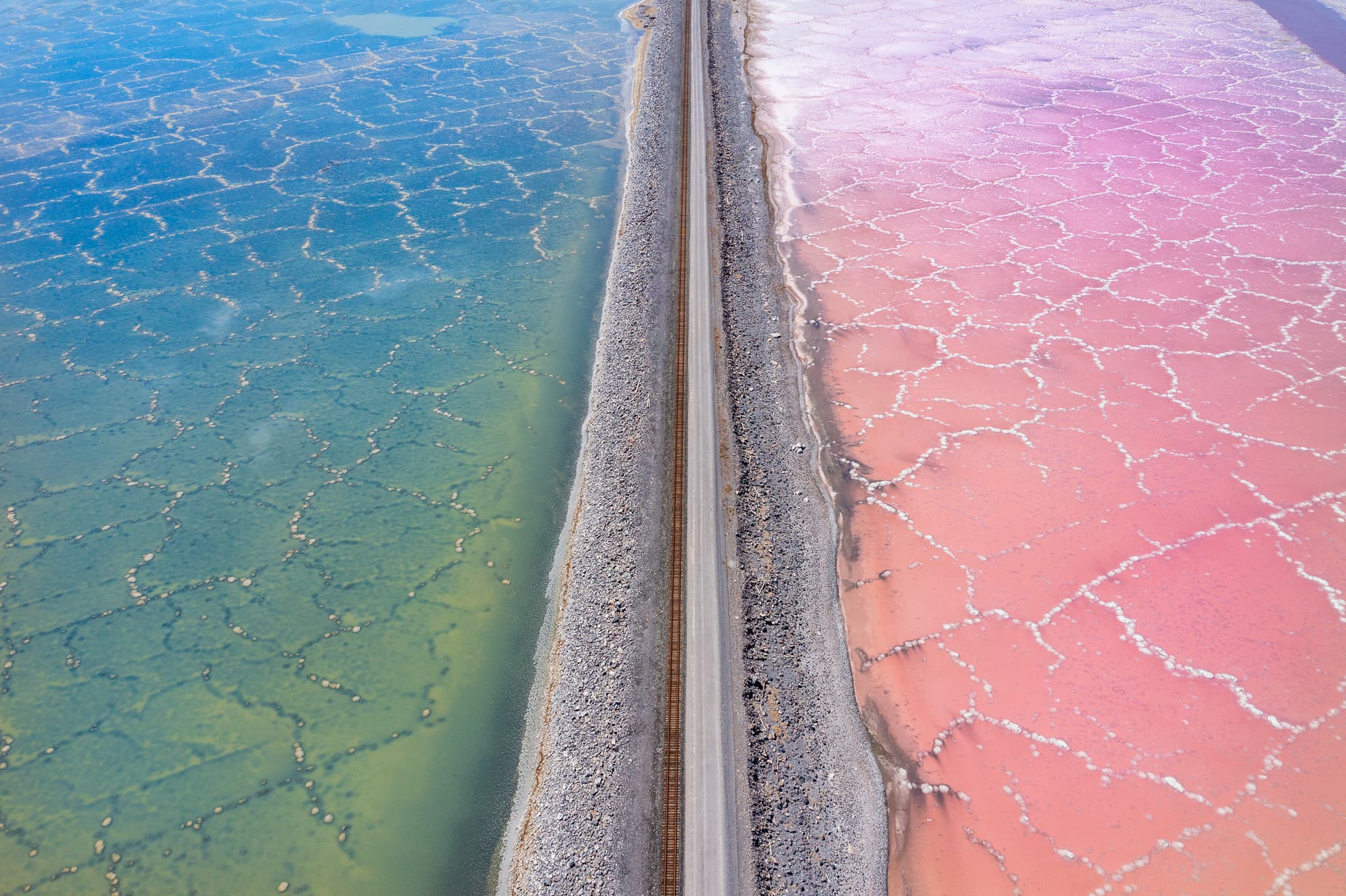 A road divides two contrasting bodies of water, with one side appearing blue-green and the other side pink